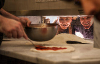 Two people watching pizza being made
