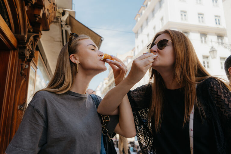 participants on a lisbon food tour eat custard tarts with their arms intertwined